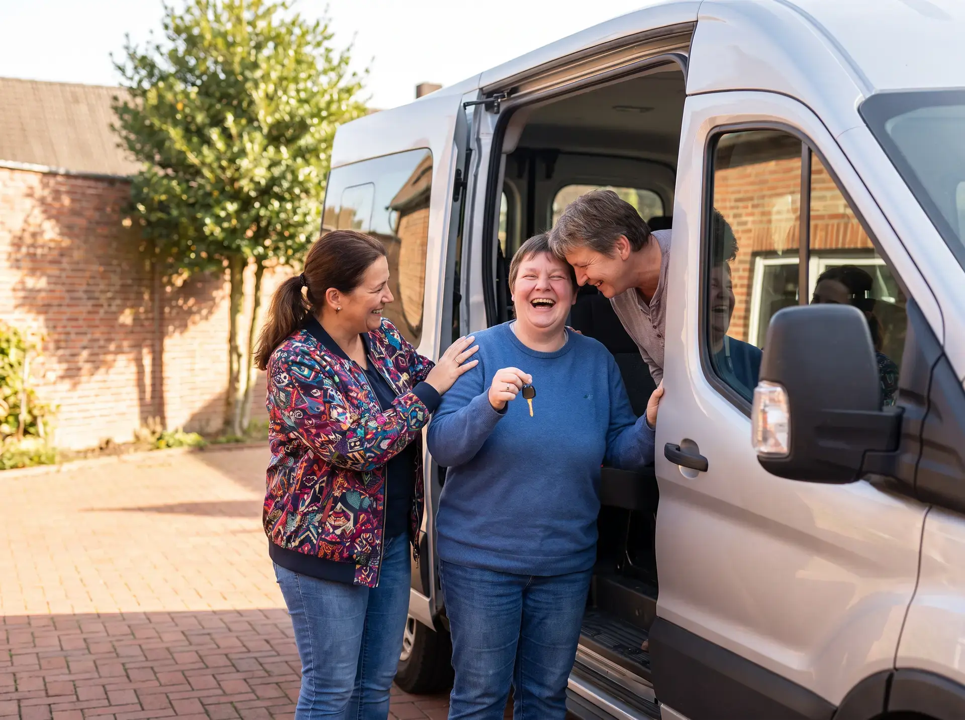 Drei Frauen stehen lachend an einem neuen Kleinbus, eine hält den Fahrzeugschlüssel in der Hand