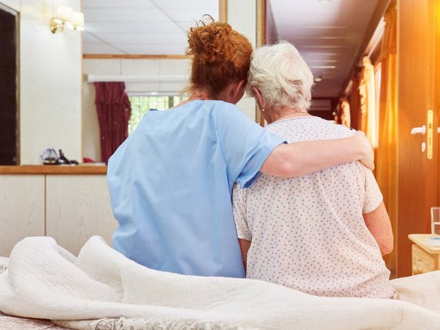 Pflegerin umarmt ältere Frau auf dem Bett sitzend